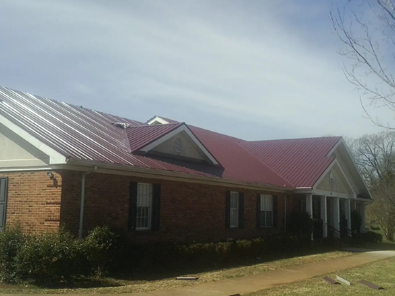 Red metal roof with gabled entries on a long brick building, from a Hail Damage Roof Repair job in Millersburg