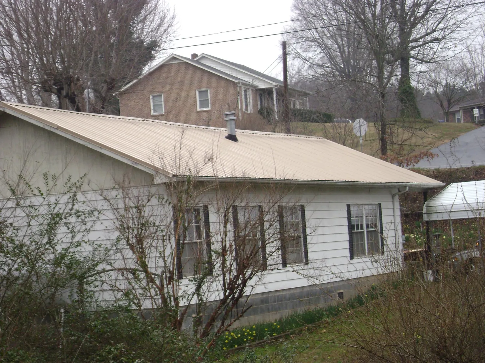 Tan metal roof on a white sided house set into a hillside — Commercial Roofing by Roofing Brothers in Millersburg